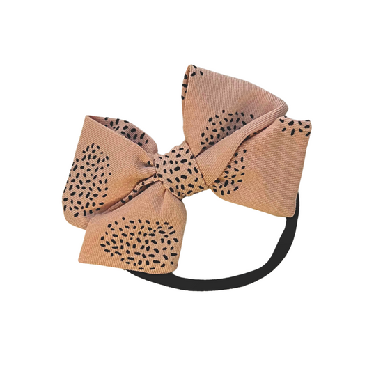 Large blush pink bow hair headband with black dot pattern on a pink background